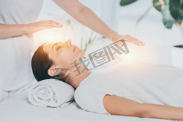 cropped shot of reiki healer doing therapy session to calm young woman with closed eyes