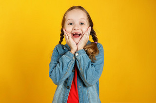 Cheerful emotional little girl in a denim shirt on a yellow background. The child is pleased with th