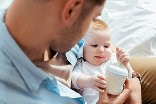 selective focus of cute baby boy touching bottle with milk in fathers hands
