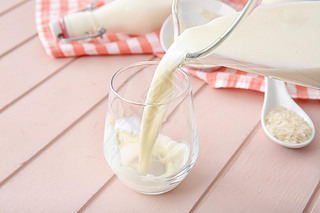 Pouring of rice milk from jug into glass on table