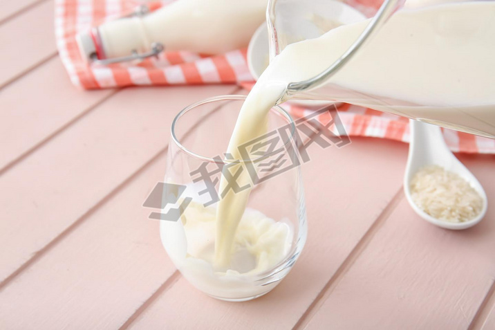 Pouring of rice milk from jug into glass on table