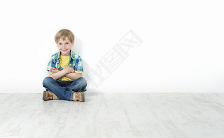 Handsome little boy sitting on floor leaning against white wall