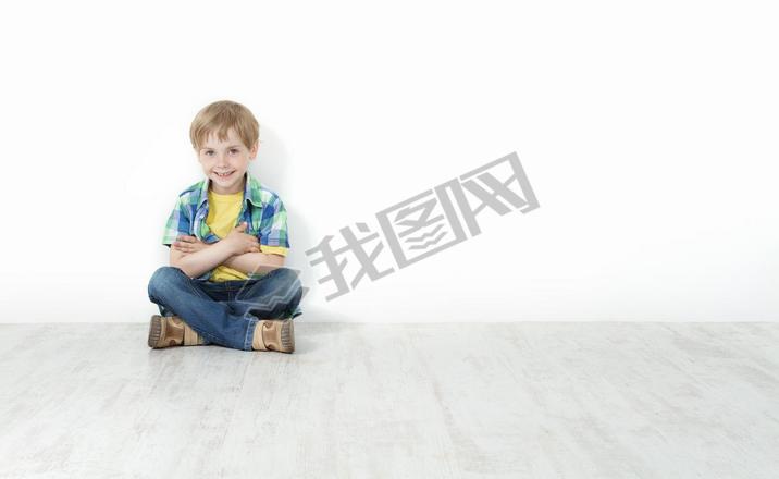 Handsome little boy sitting on floor leaning against white wall