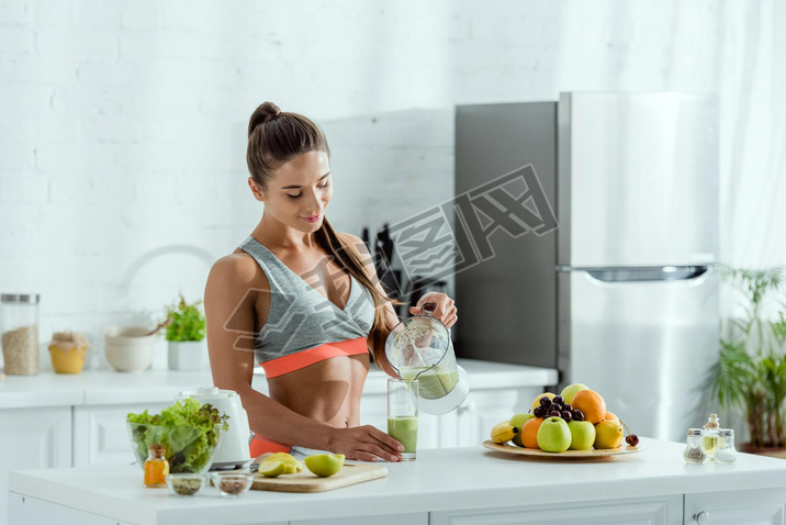 happy girl with sportswear pouring oothie in glass from blender 