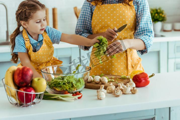 mother in polka dot yellow apron giving daughter sliced lettuce