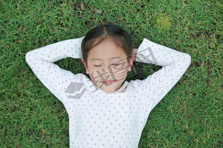 Close-up Asian little child girl iling with hands behind head and closed eyes resting on green gra