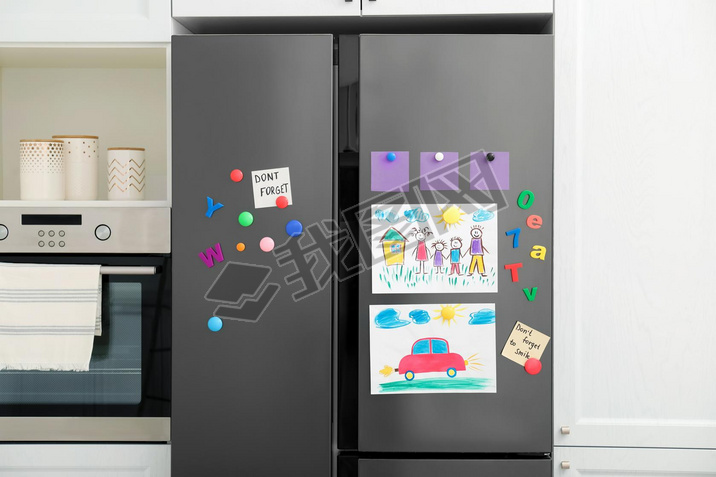 Modern refrigerator with child's drawings, notes and magnets in kitchen