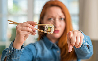 Redhead woman eating sushi using chopsticks pointing with finger to the camera and to you, hand sign