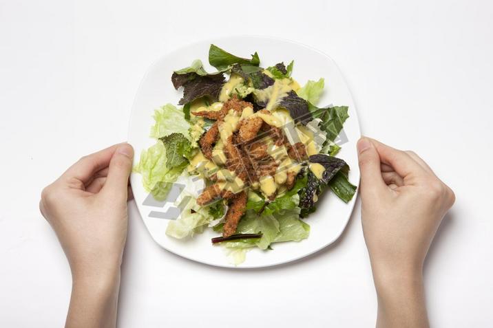 Woman hand hold a dish with salad on the white table.