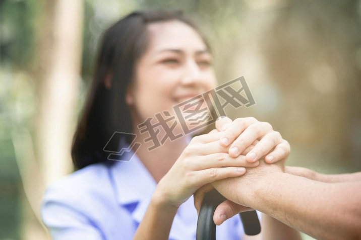 Comforting hand. Young nurse holding old man's hand in outdoor garden sitting on bench. Senior care,