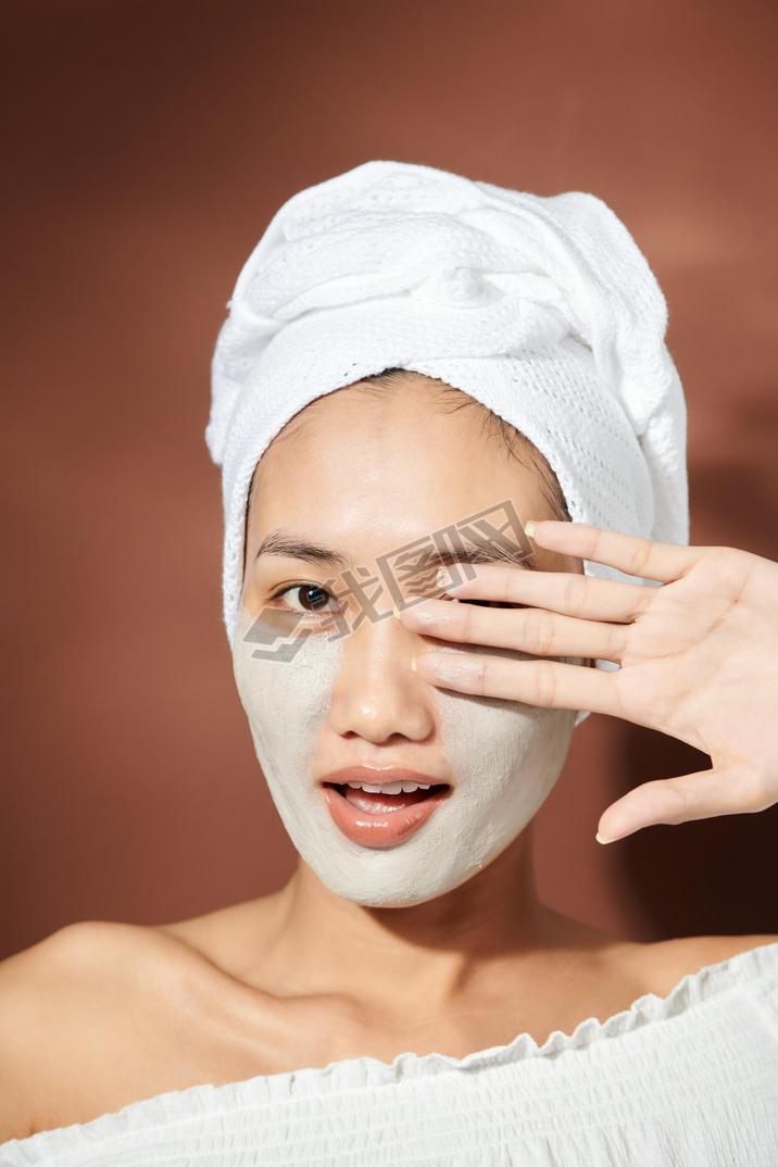 Close up shot of beautiful Asian woman applies purifying mask on face, has beauty treatments