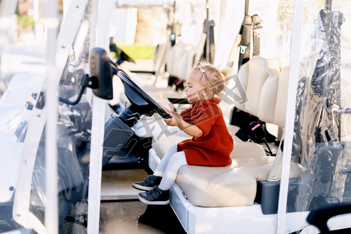 Cute 2-year old is sitting in the drivers seat of a golf cart
