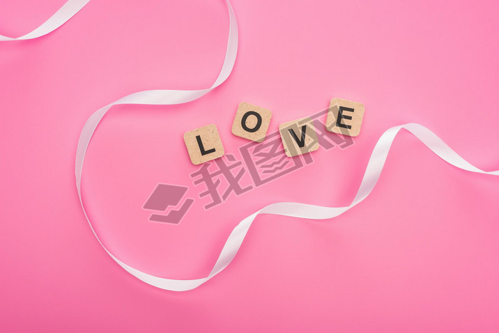 top view of curved ribbon and wooden blocks with love lettering isolated on pink