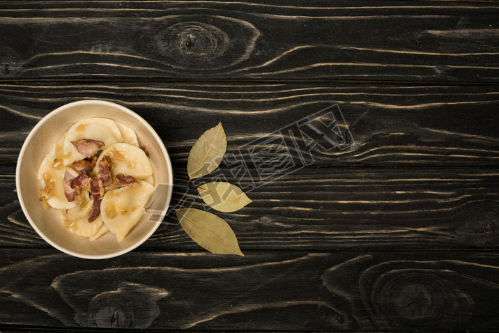 top view of delicious varenyky with cracklings in bowl near bay lees on black wooden table