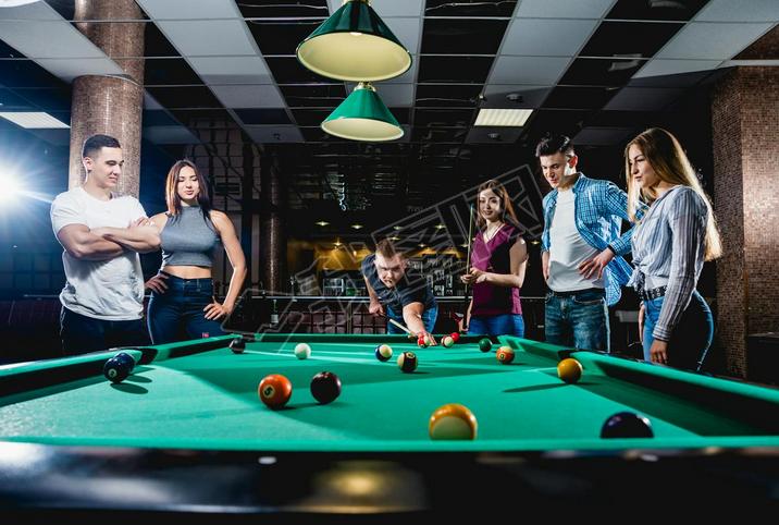 Group of young cheerful friends playing billiards. Funny time after work