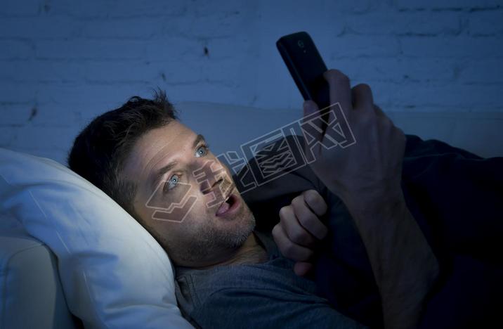man in bed couch at home late at night using mobile phone in low light watching online porn