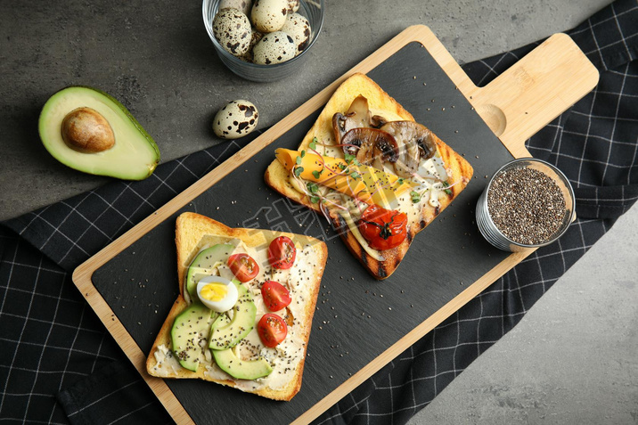 Different toasts with ocado, mushrooms, cherry tomatoes and chia seeds served on grey table, top v