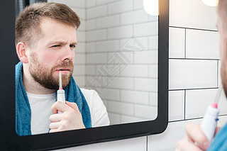 Serious man brushing his teeth with an electric oral irrigator with a jet of water, looking in the m