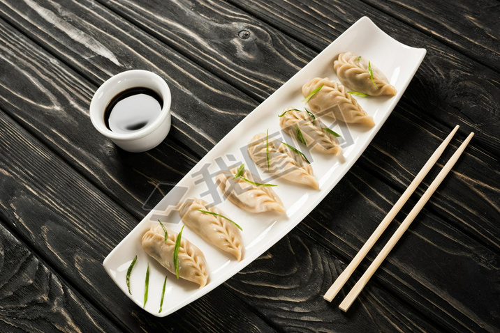 delicious Chinese boiled dumplings on plate near chopsticks and soy sauce on black wooden table