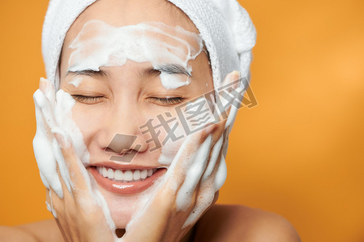 Gentle half-naked woman wrapped in towel washing her face with f