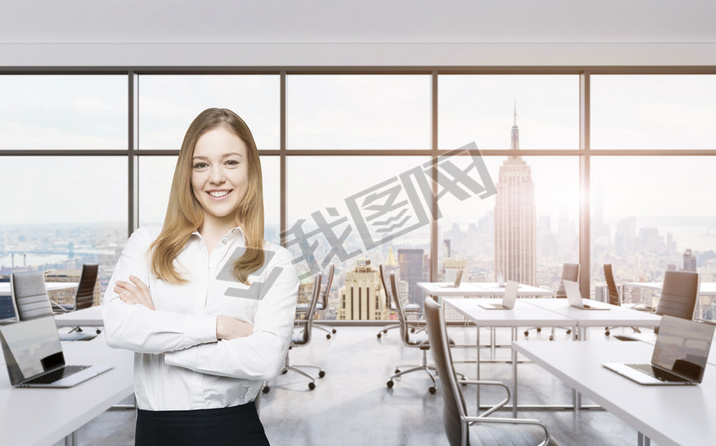 Smiling beautiful business lady with cross hands is standing in a modern panoramic office in New Yor