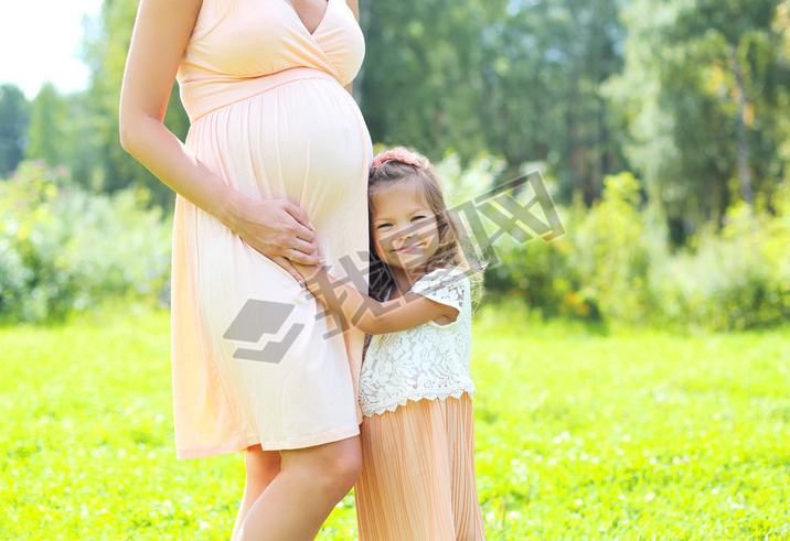 Happy pregnant woman, cute little child daughter hugging mother