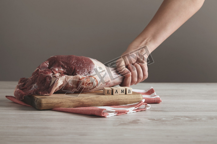Hand holds raw lamb leg meat on table