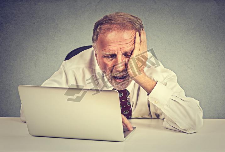 Tired sleepy senior man sitting at his desk in front of laptop computer