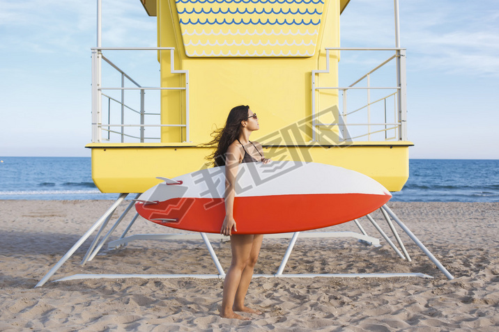 Woman standing with surfboard near the lifeguard house