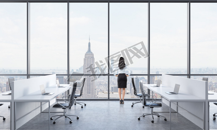 Rear view of a brunette who is looking out the window in the modern panoramic office with New York v