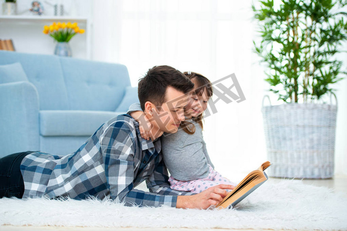 Cute little girl listening to dad reading fairy tale lying on warm floor together, caring father hol