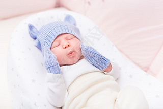 Cute little baby wearing knitted blue hat with ears and mittens lying in beautiful cradle with close