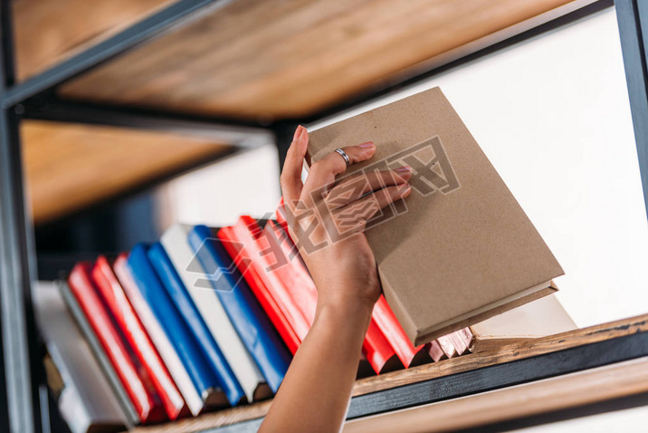 Cropped shot of student holding book at bookshelf in library 