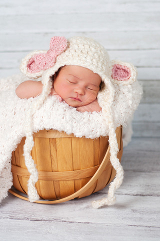 Newborn girl wearing a crocheted lamb hat and sitting in a basket