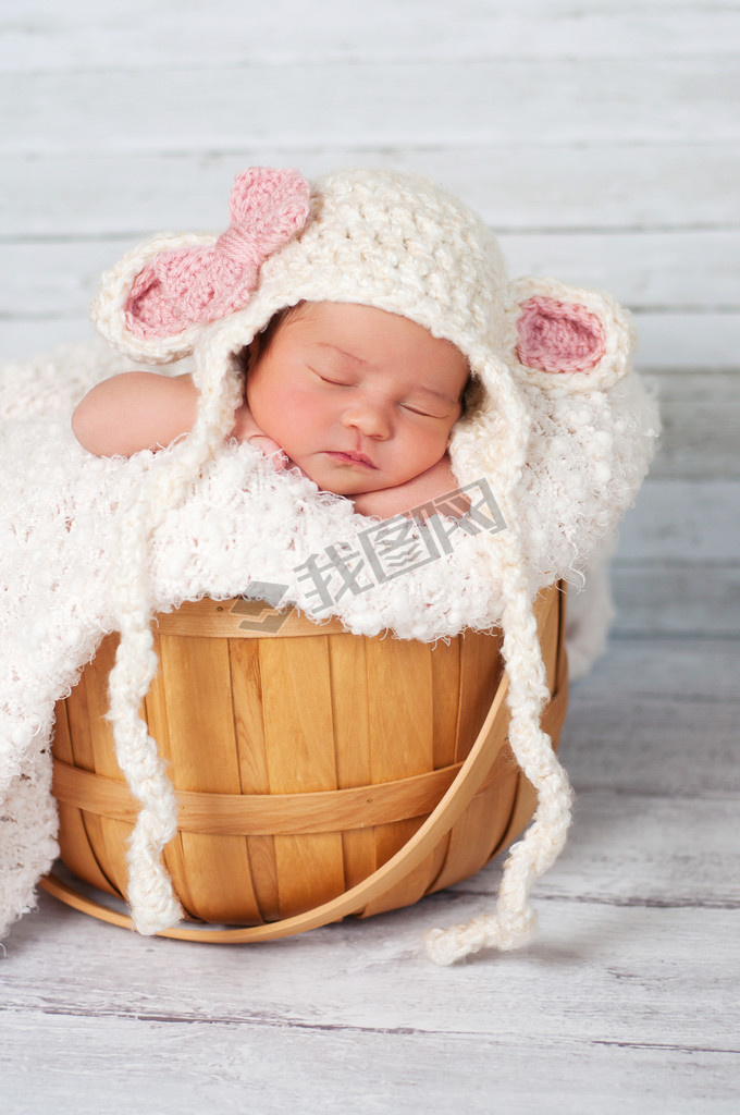 Newborn girl wearing a crocheted lamb hat and sitting in a basket