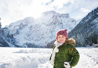 Happy child in green coat standing in front of snowy mountains