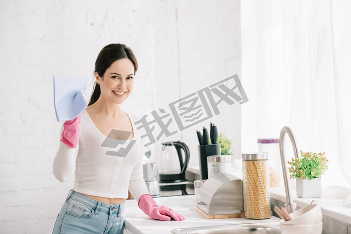 happy housewife looking at camera while standing in kitchen and holding rag