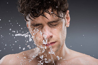 handsome man washing face with water in the morning, isolated on grey