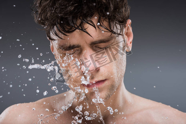 handsome man washing face with water in the morning, isolated on grey