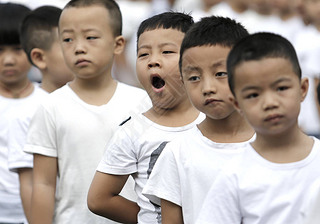 A young student yawns as he and other students attend a flag-raising ceremony of a new semester at a