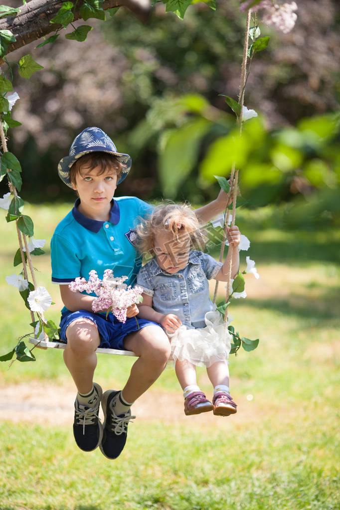 brother and sister swinging on swing in summer park, outdoor