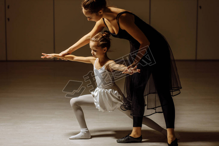 young ballerina woman training little girl in ballet studio