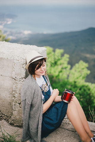 Young fashion woman sitting on a top of the mountain drinking tea