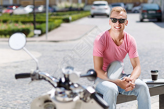 Handsome man sitting with coffee near his scooter