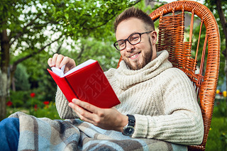 Handsome man relax in rocking-chair  reading red book in summer garden.