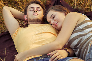 Loving couple lying down on floral field in autumnal park, warm sunny day, enjoying family, romantic