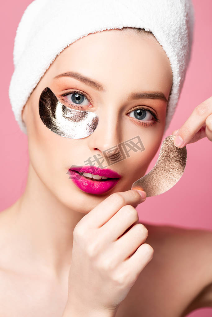 beautiful woman in while towel applying eye patches isolated on pink 