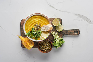 top view of delicious mashed pumpkin soup on wooden cutting board on marble surface with ingredients