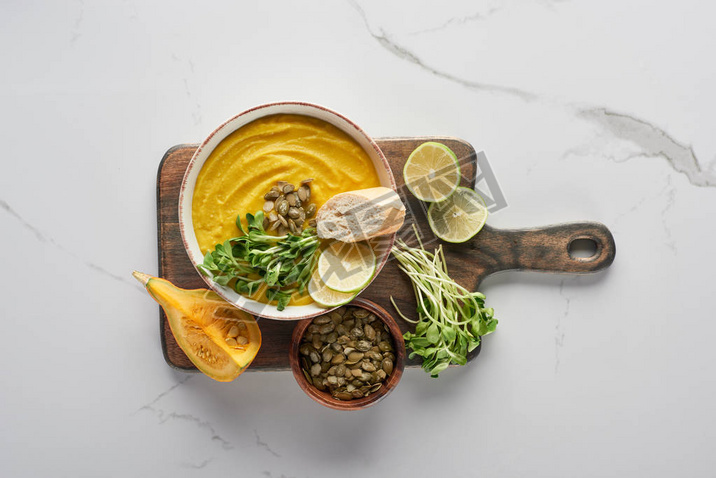 top view of delicious mashed pumpkin soup on wooden cutting board on marble surface with ingredients