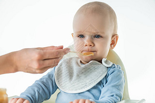 Selective focus of mom feeding adorable baby boy with fruit baby nutrition isolated on white